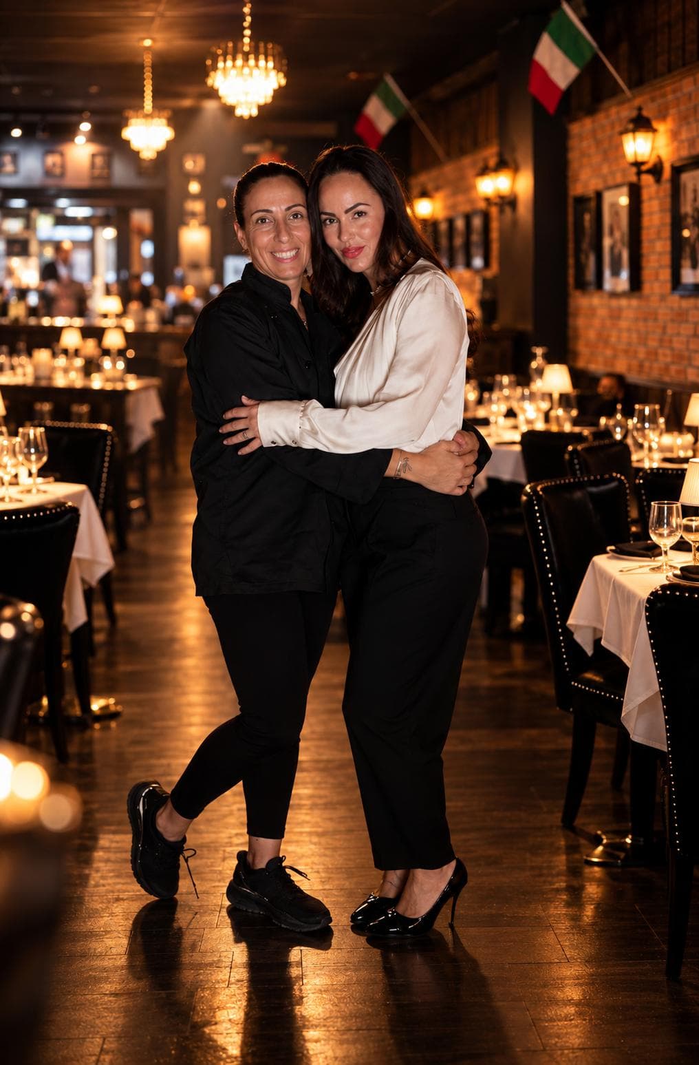 Two women embracing in the dining room, one in a black chef's jacket, the other in a cream silk blouse