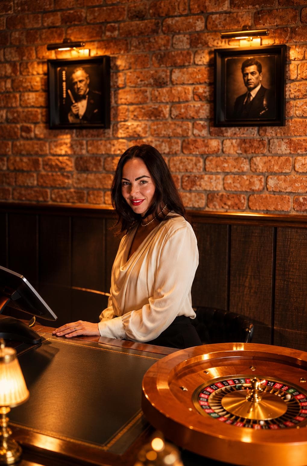 A woman in a cream silk blouse at the front desk under portraits of film gangsters, a roulette wheel in the foreground